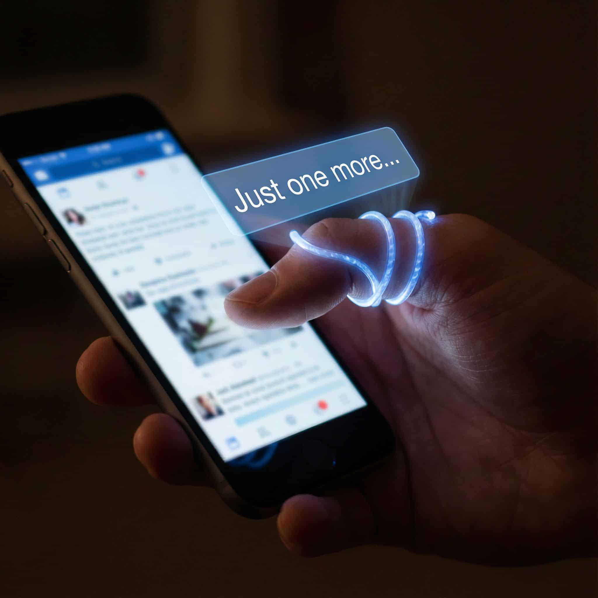 손가락을 휘감은 빛나는 알림 배너가 "한 번만 더..."라고 표시되며 휴대폰을 쥔 손을 조종하는 모습이다.